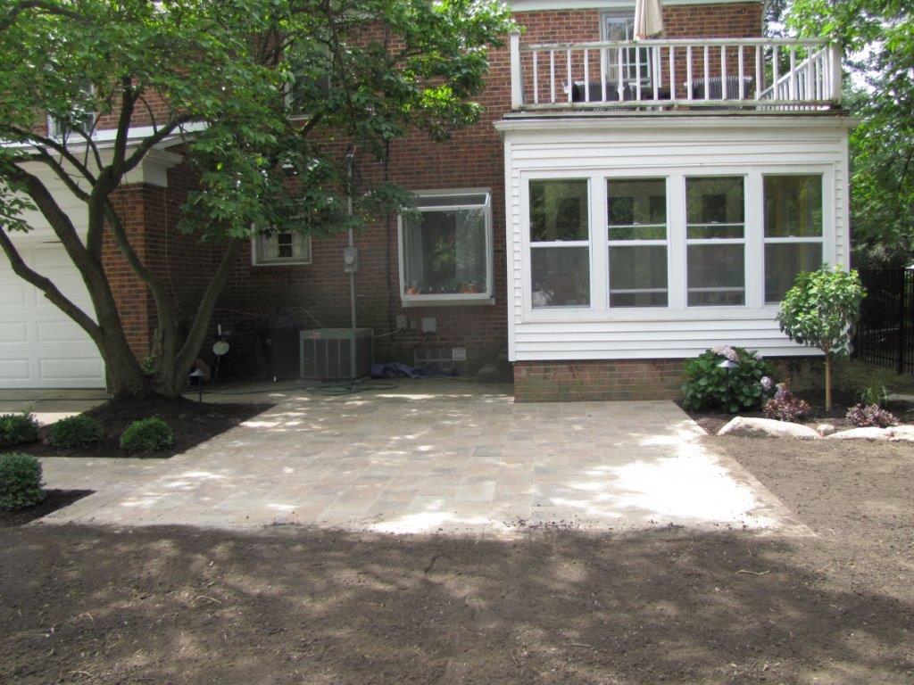 Back patio with concrete slab, brick house, white-trimmed windows, and a small balcony above