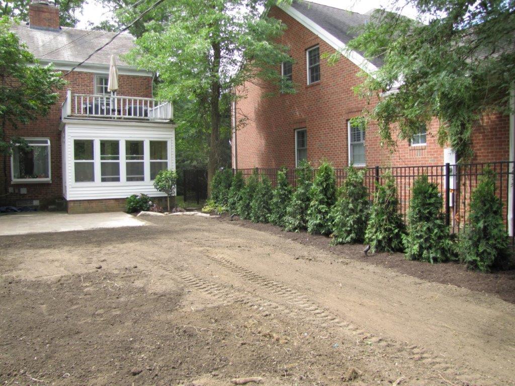 Brick house with white sunroom and gravel driveway, lined by tall hedges and trees