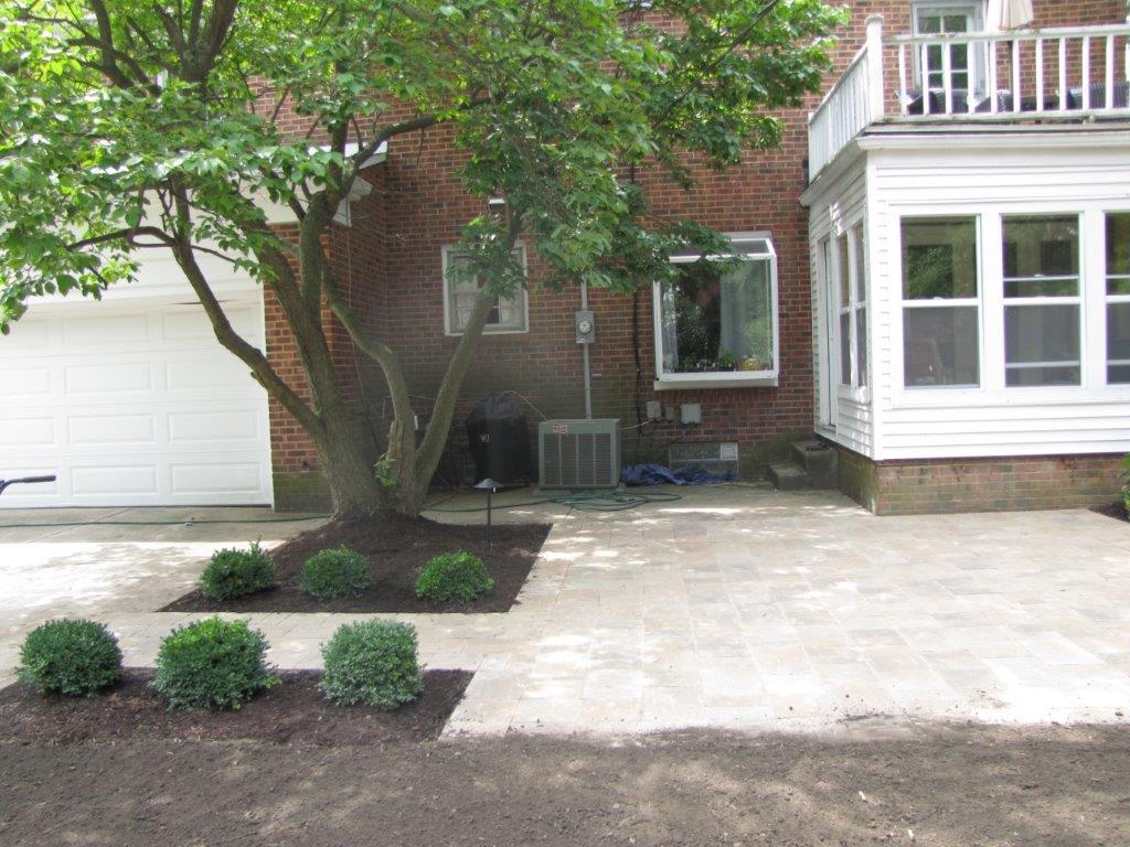 Front driveway and brick house with white garage, tree, and landscaped garden beds