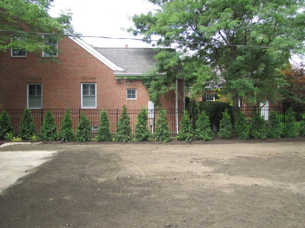 Brick building with white-trimmed windows, trees, and a gravel courtyard in front.