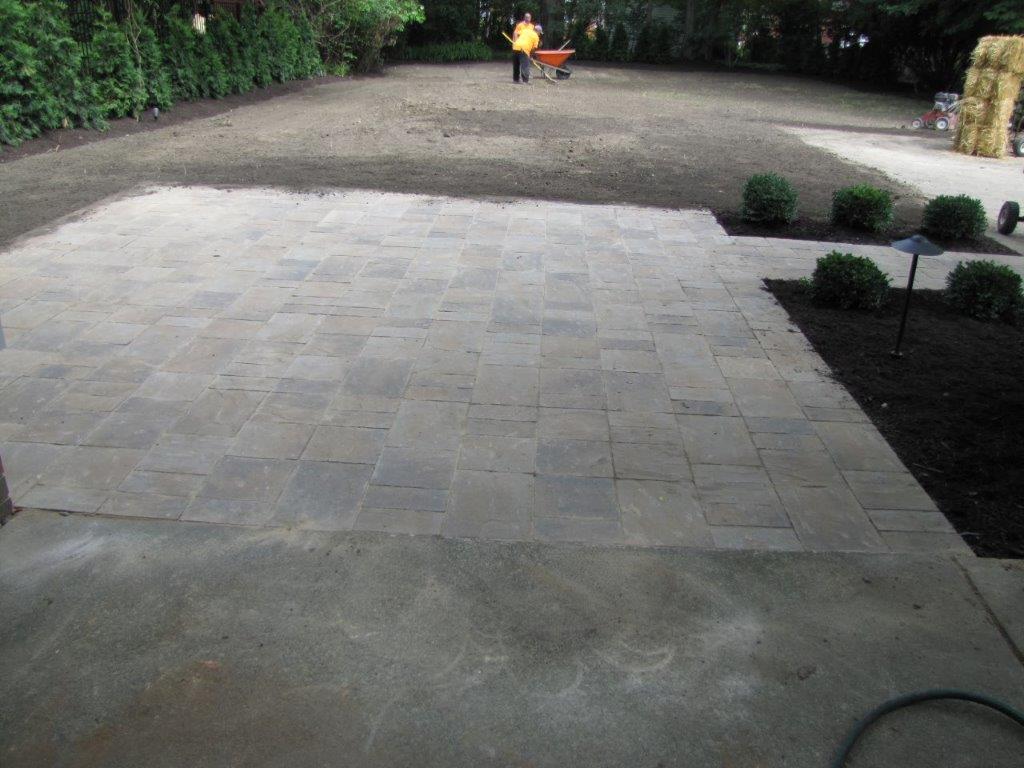 Patio with light stone pavers, dark mulch beds, and a wheelbarrow in the distance