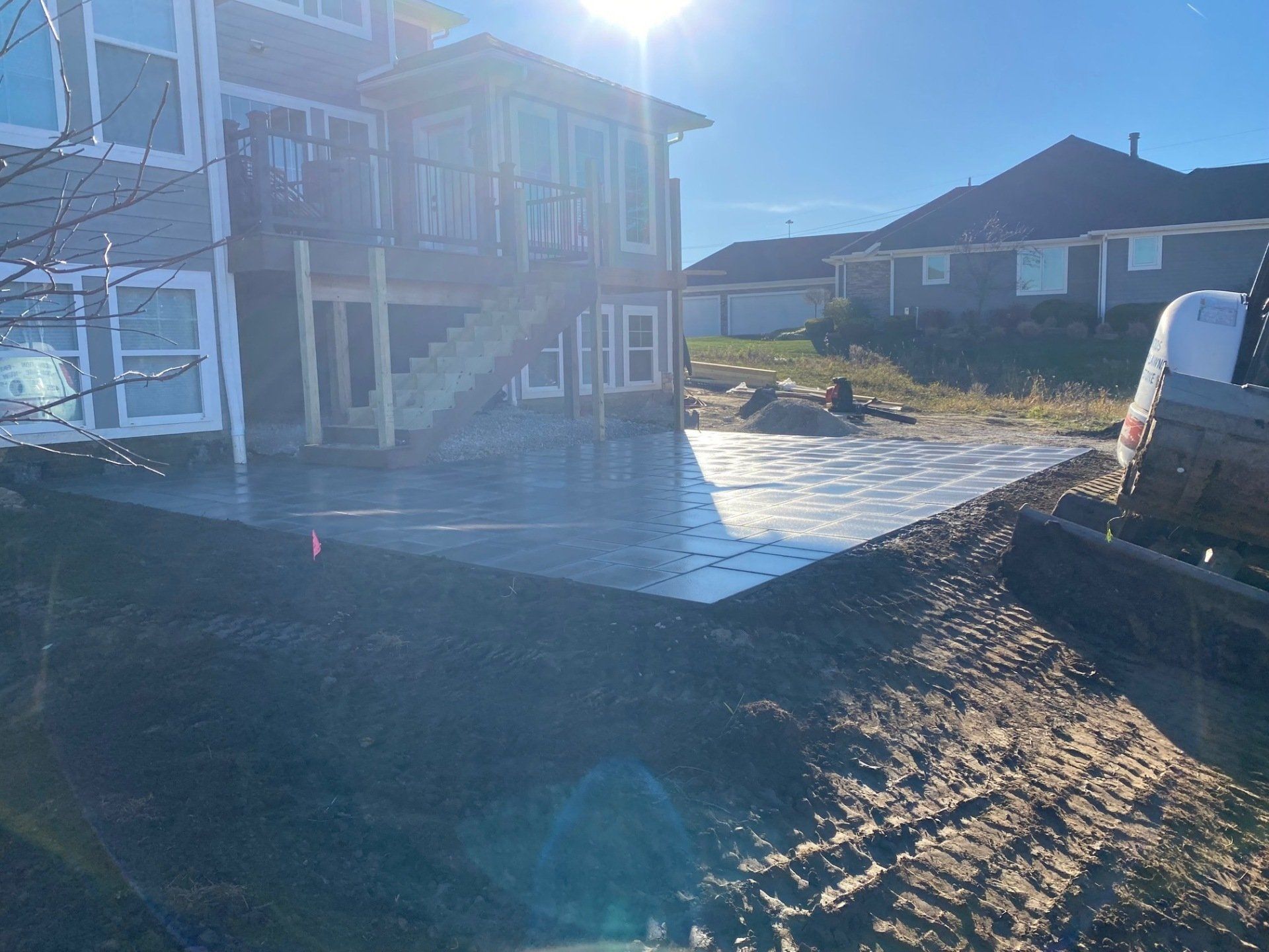 House under construction with concrete foundation, muddy yard, and a parked vehicle in bright sun