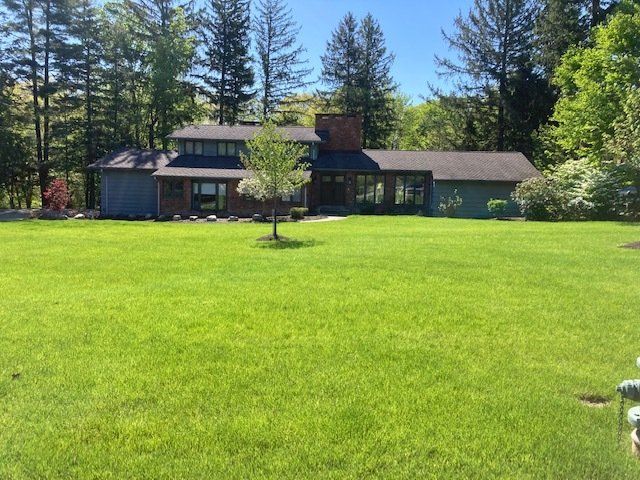 House with a green lawn and tall trees on a sunny day