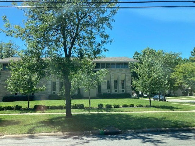 Large brick building with white columns behind a grassy lawn and trees under a bright blue sky