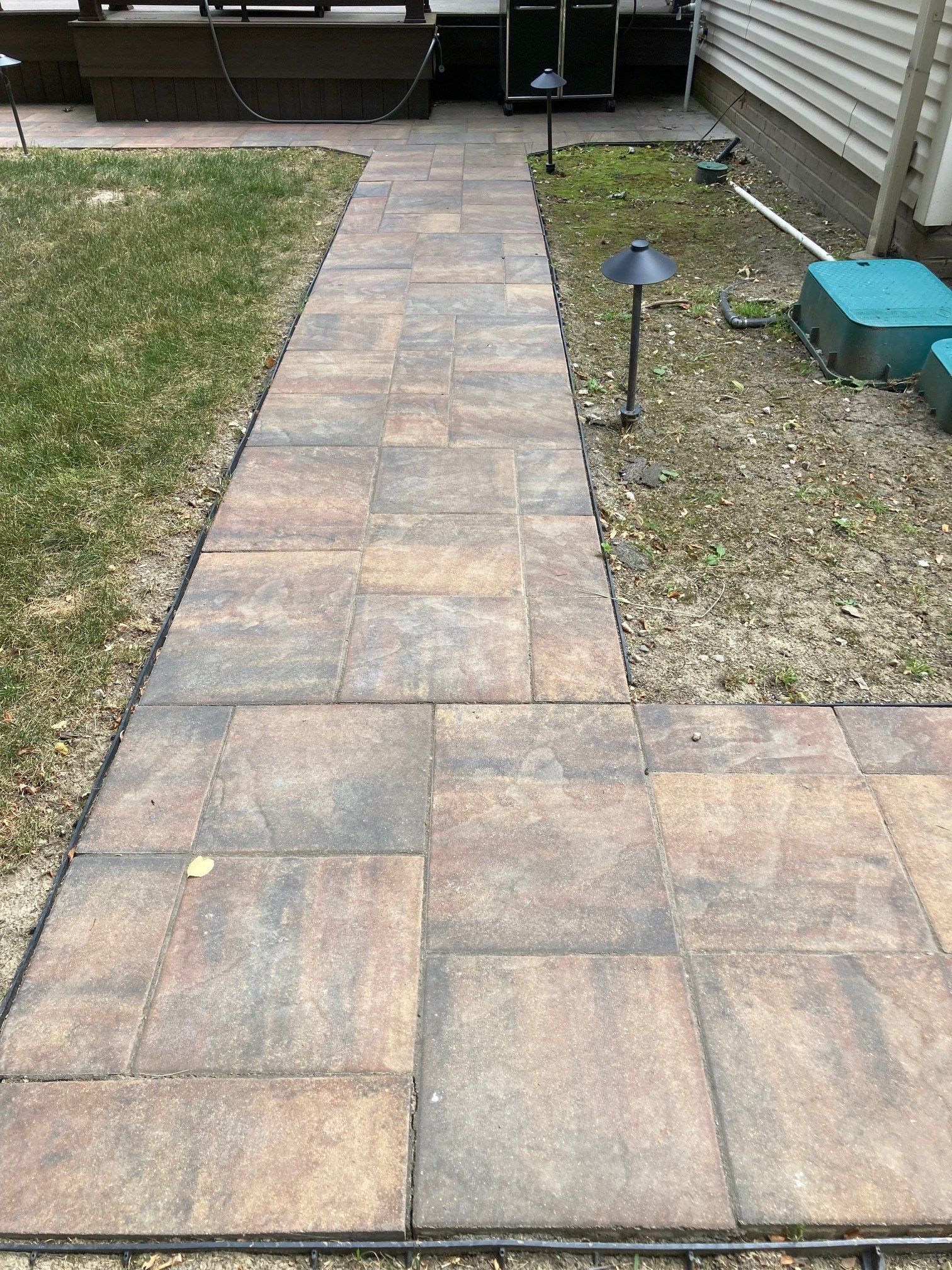 Brick paver walkway leading to a patio, bordered by grass and mulch with a small garden light.
