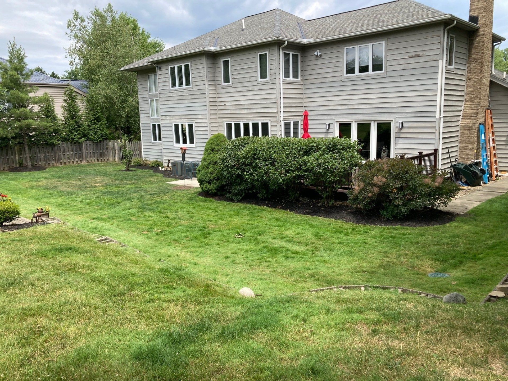 Suburban house with white siding, stone chimney, and a green lawn under overcast skies