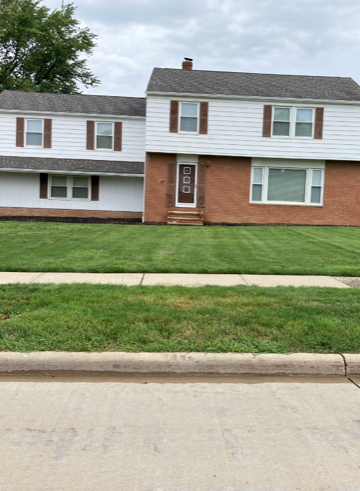 Suburban duplex with white siding and brick fronts, viewed from the street across a green lawn.