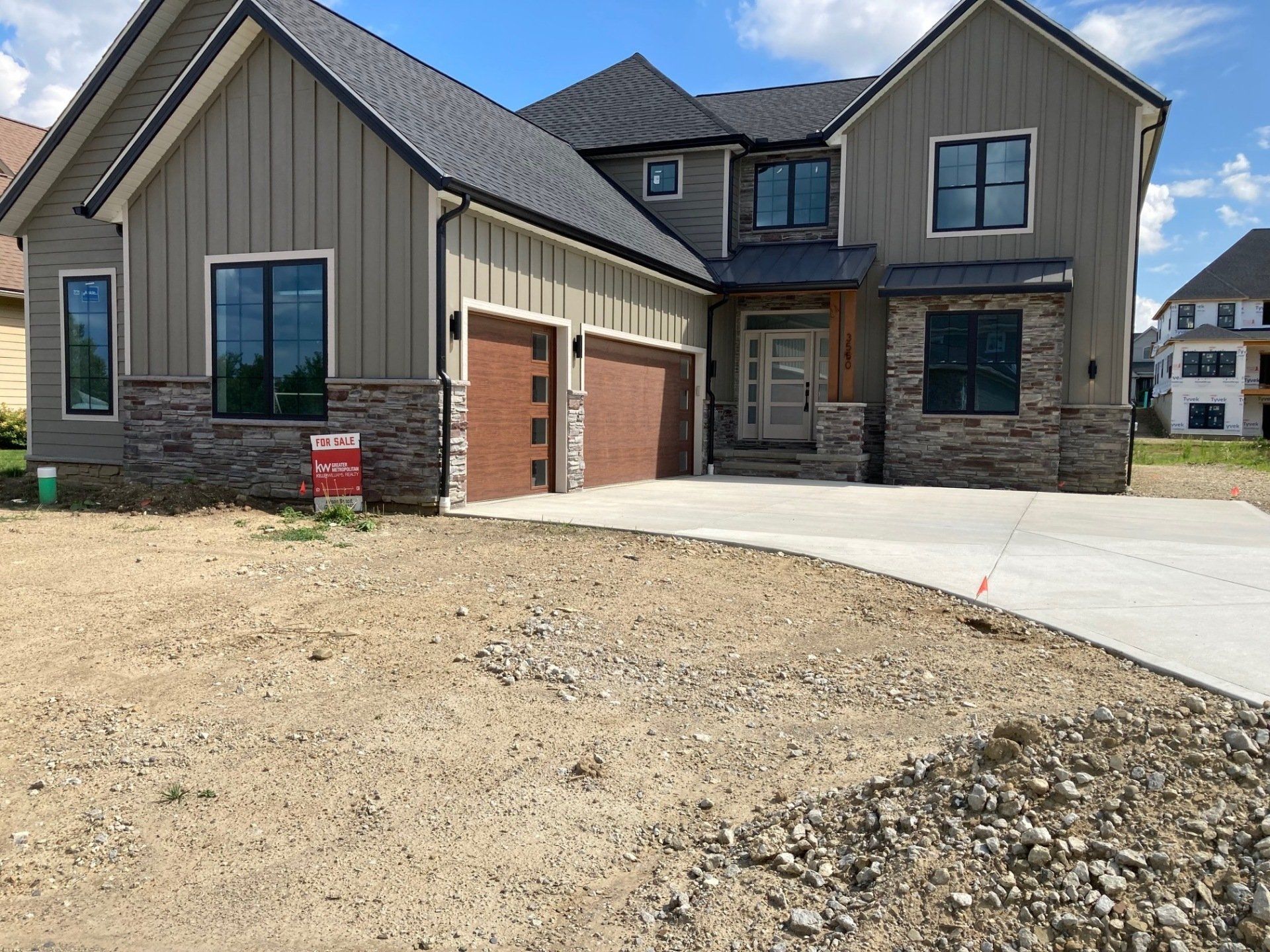 New suburban house with stone and gray siding, two-car garage, and unfinished dirt front yard