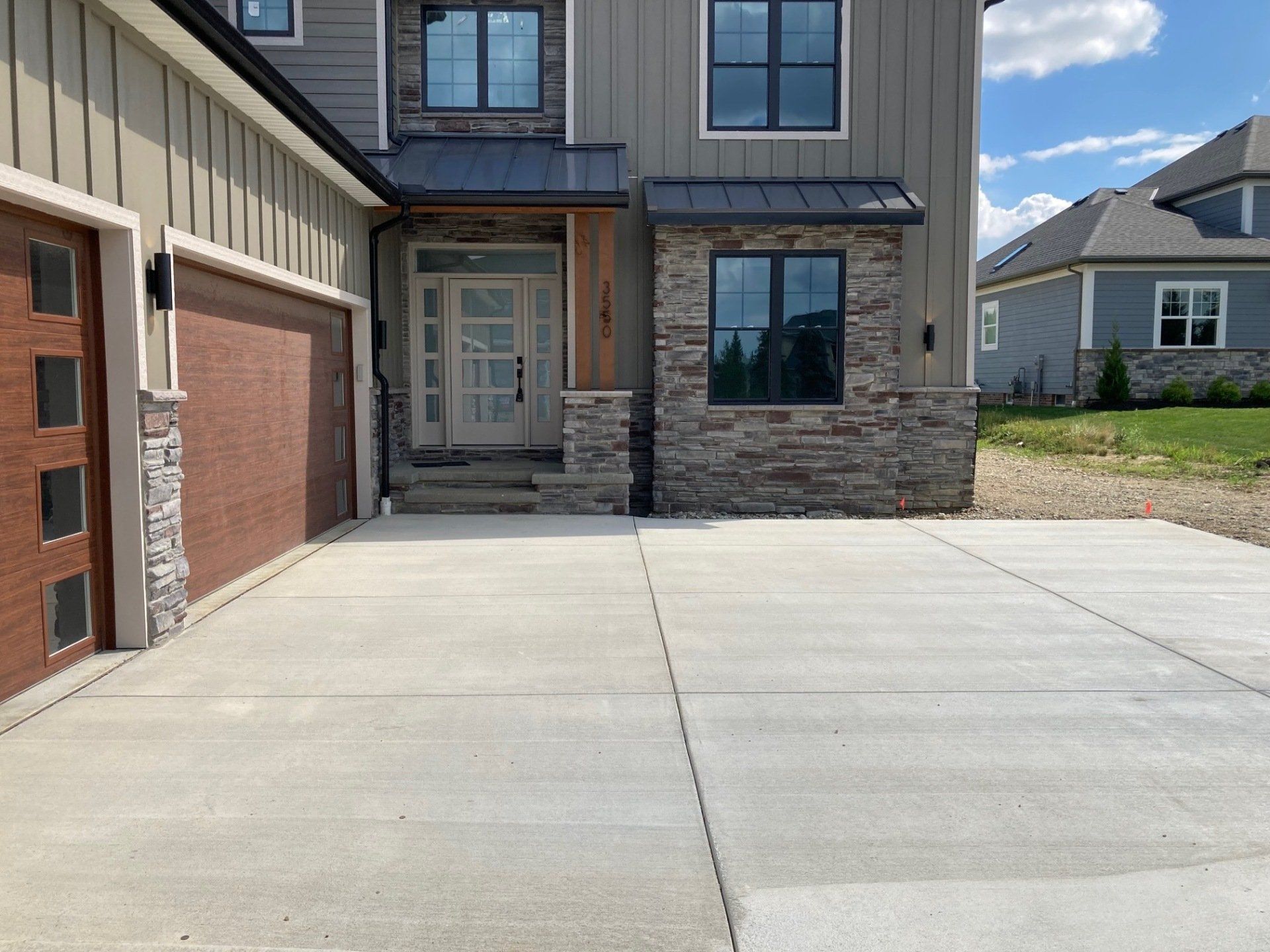 Suburban house front with stone entry, garage, and wide concrete driveway under a blue sky