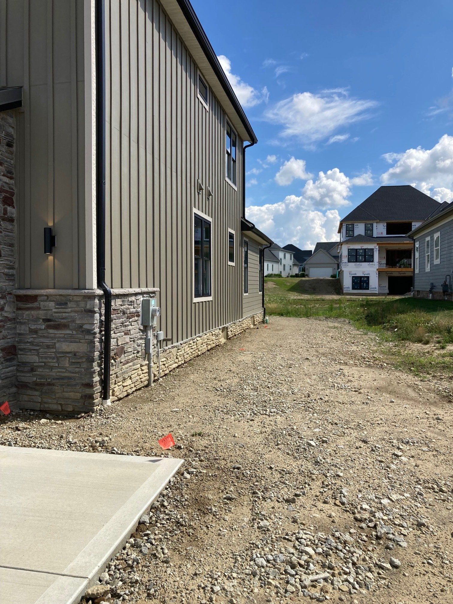 Gravel side yard beside a beige house, with new apartments in the background under a blue sky.