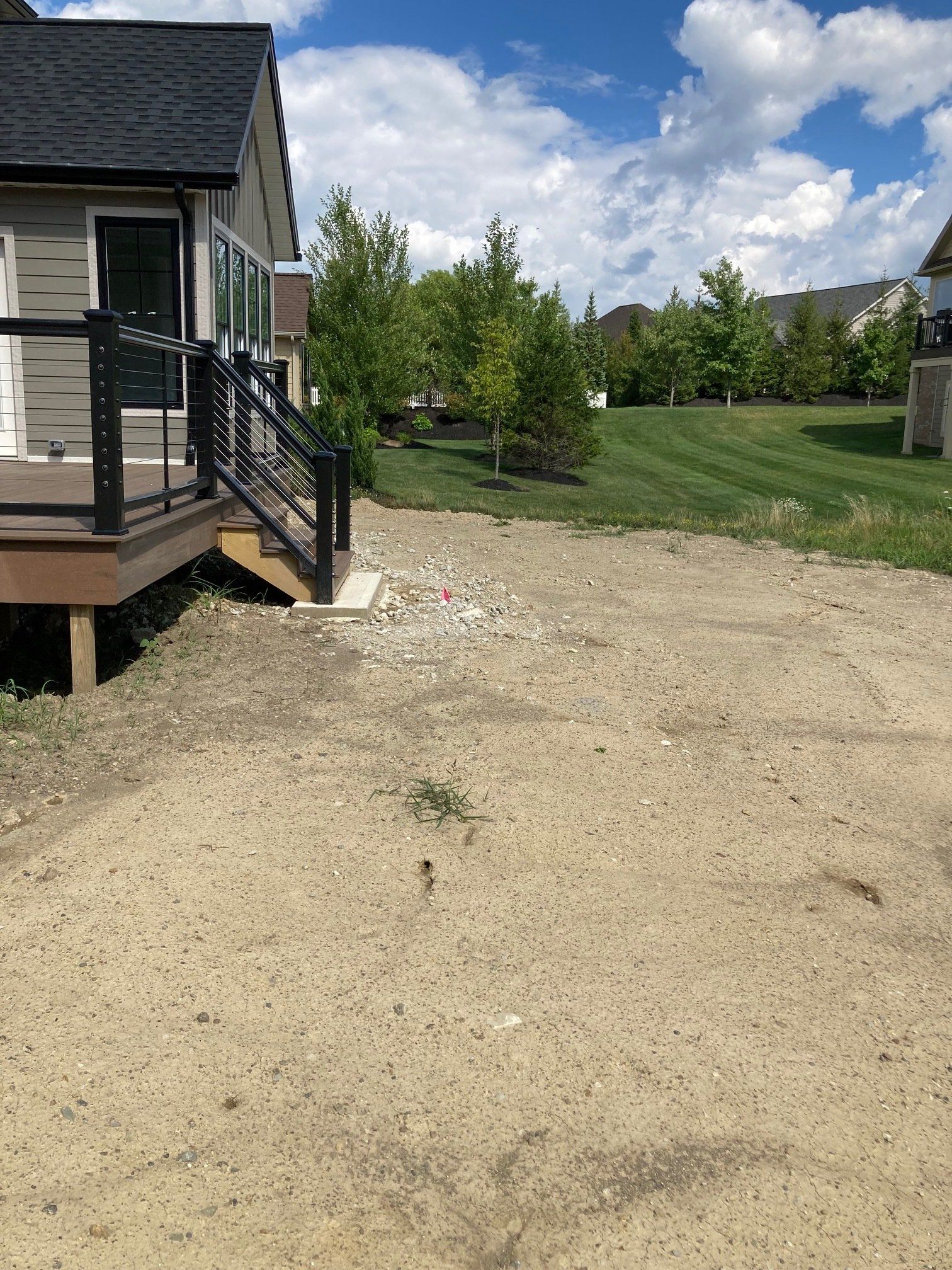 Gravel driveway beside a house with a porch and stairs, leading to a grassy yard under a partly cloudy sky