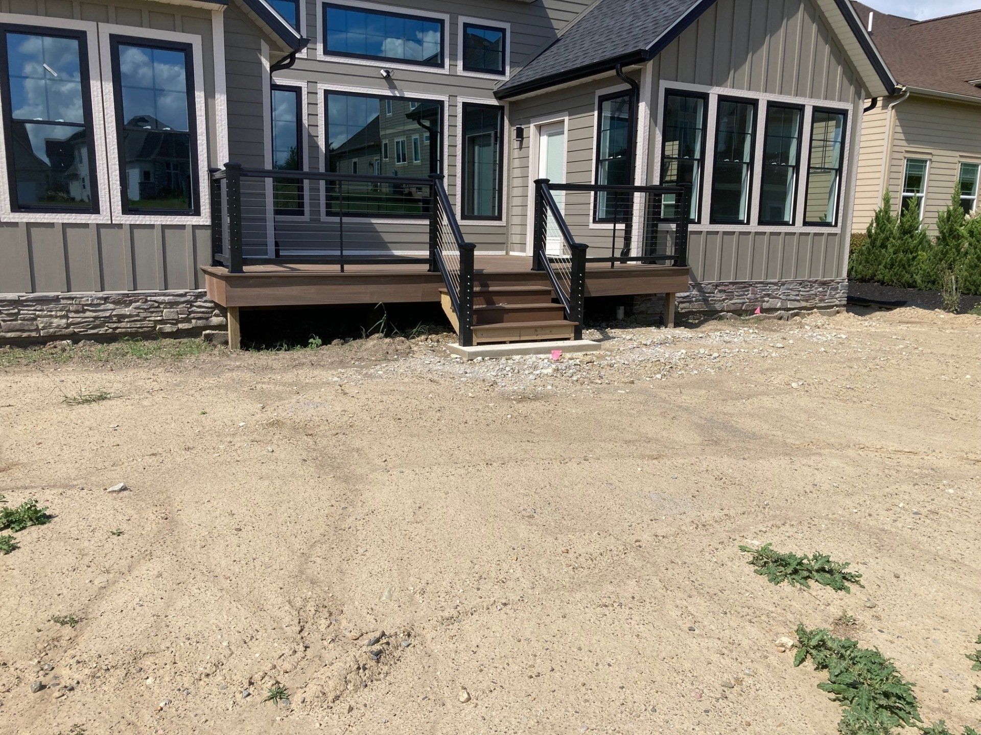 Back patio with steps, black railing, and tan siding beside a gravel yard.