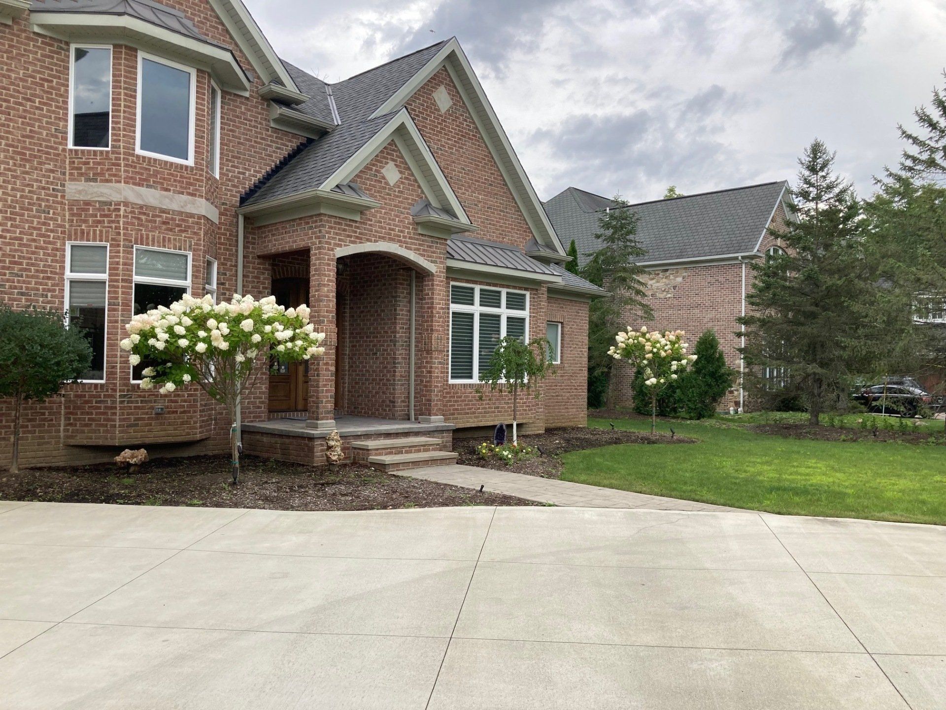 Brick suburban house with a covered entry, white flowers, and a wide concrete driveway