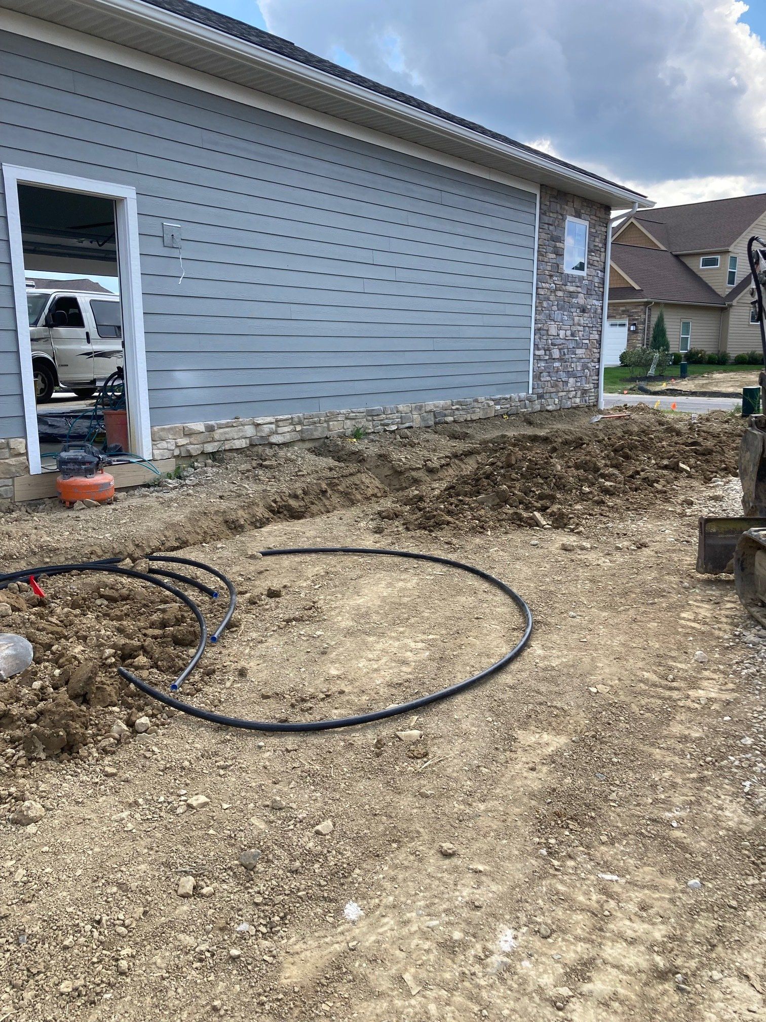 Partially landscaped yard beside a gray house, with dirt ground, coiled hose, and construction debris.