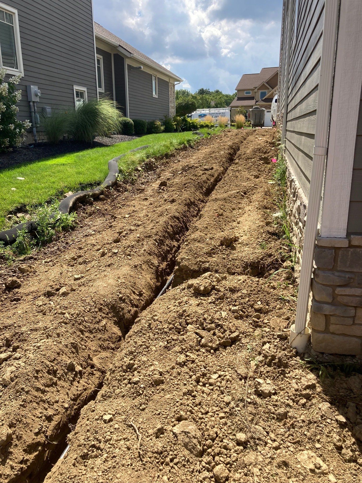 Freshly dug trench running through a narrow side yard beside two suburban houses