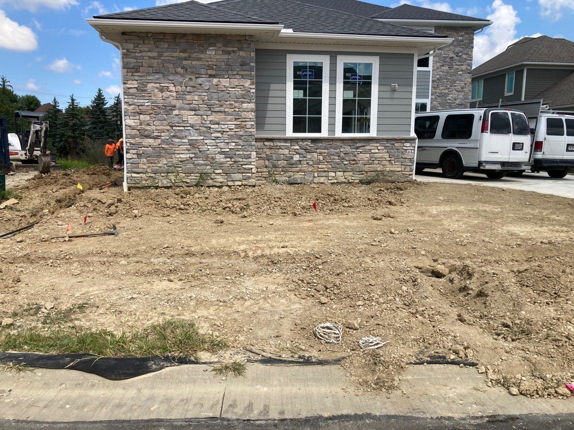 Stone-front house with unfinished dirt front yard and two white vans parked beside it