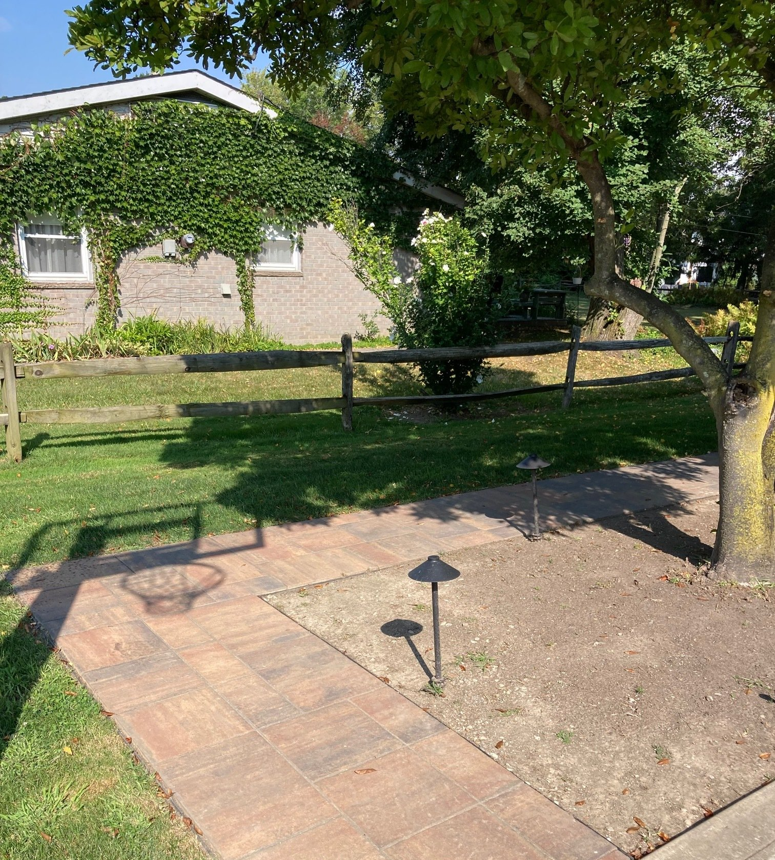Backyard patio with paved path, young tree, and low fence beside a brick house