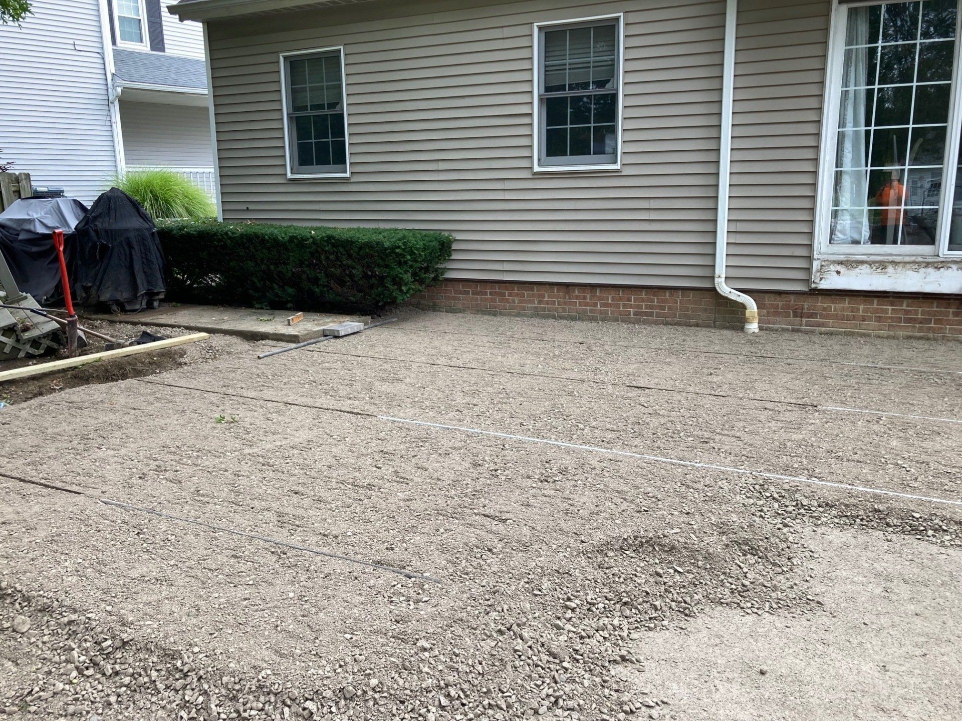 Gravel driveway beside a beige house with two windows, a door, and trimmed shrubs