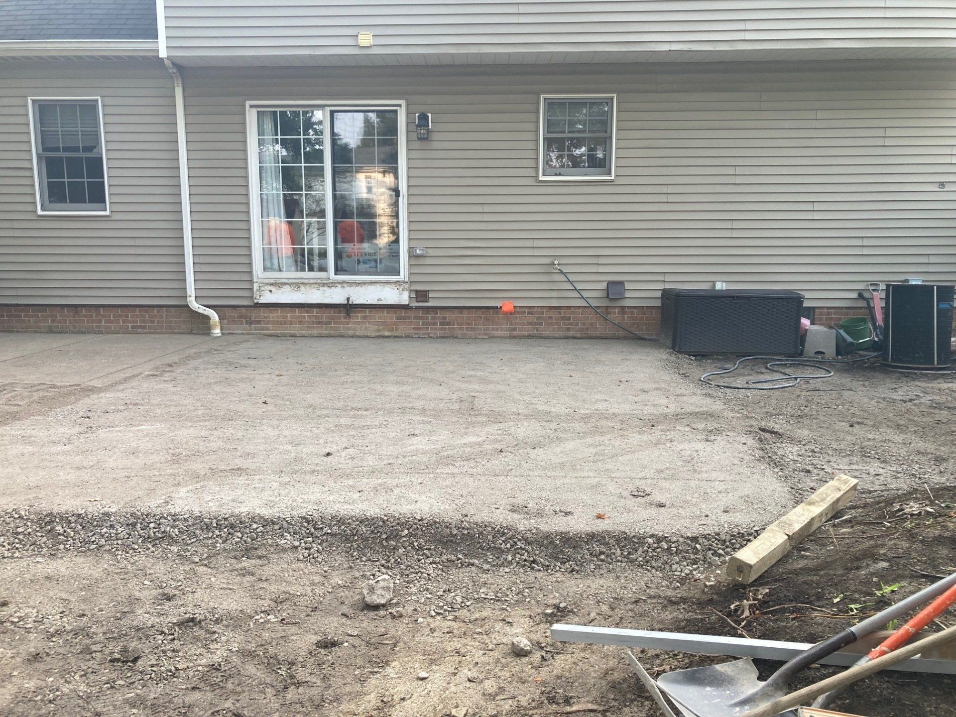 Backyard patio under construction beside a beige house with sliding glass doors and concrete forms