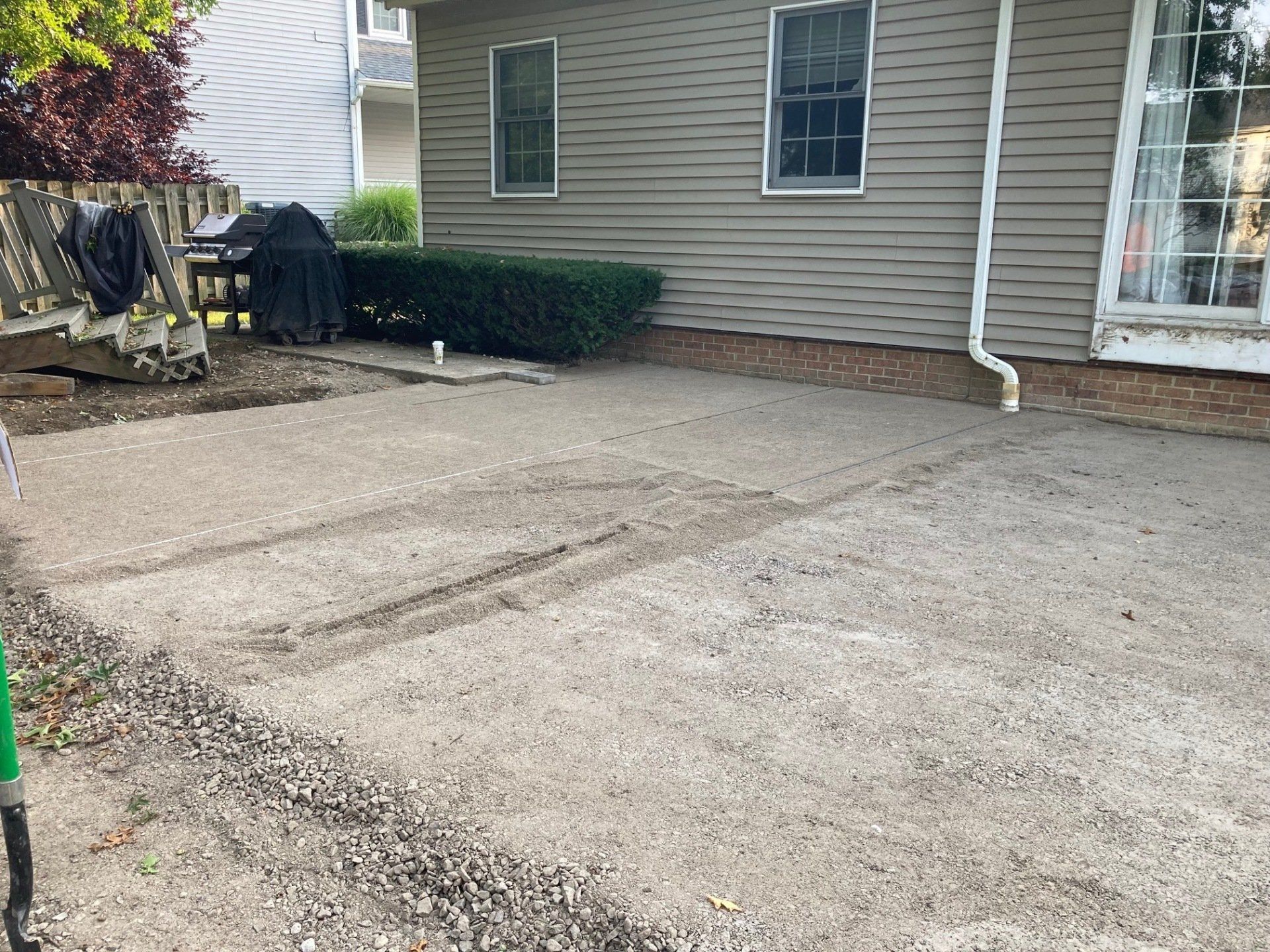 Empty gravel driveway beside a beige house with a small patio and white downspout