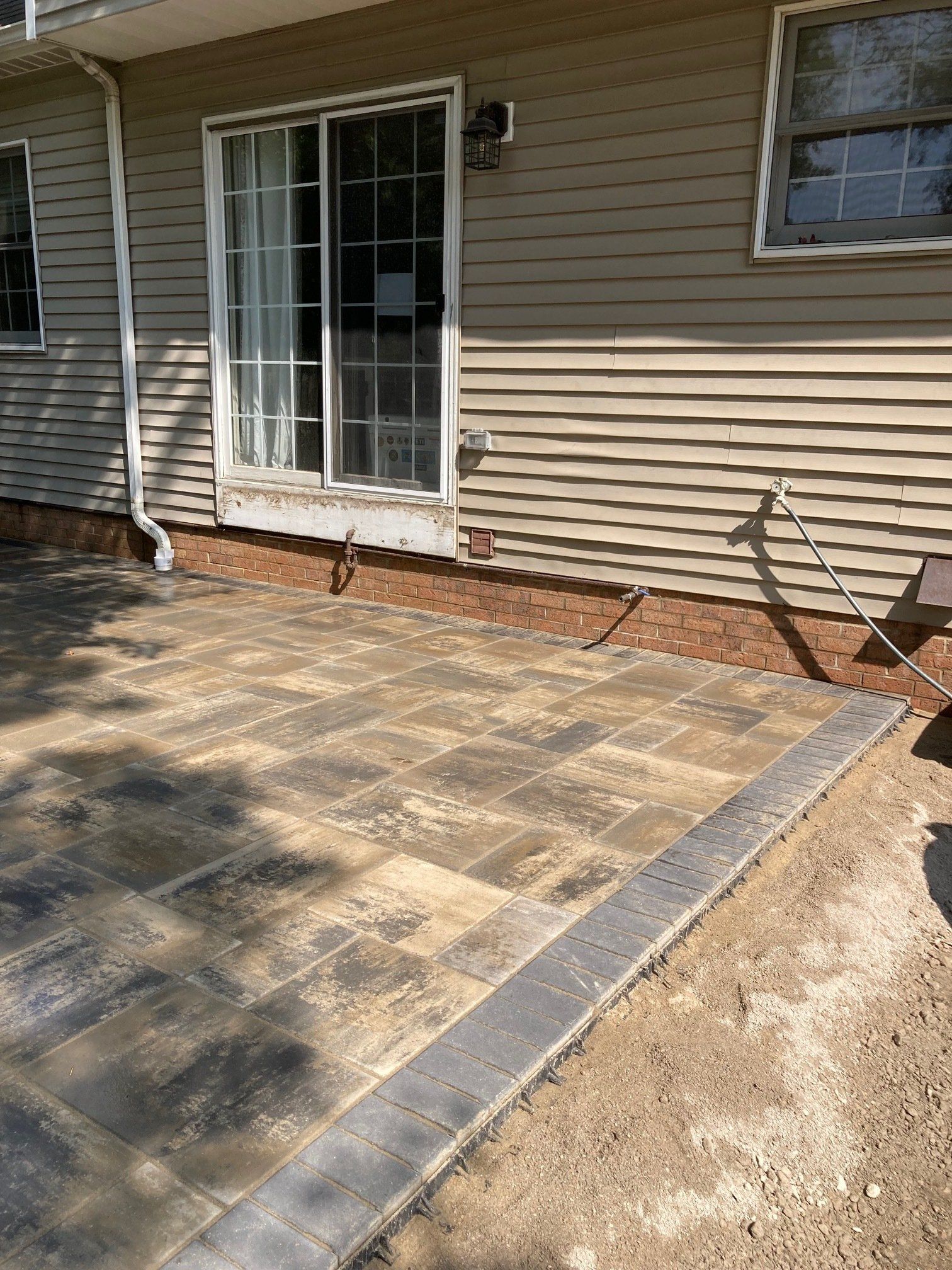 Stone patio beside a beige house with sliding glass doors and a small window.