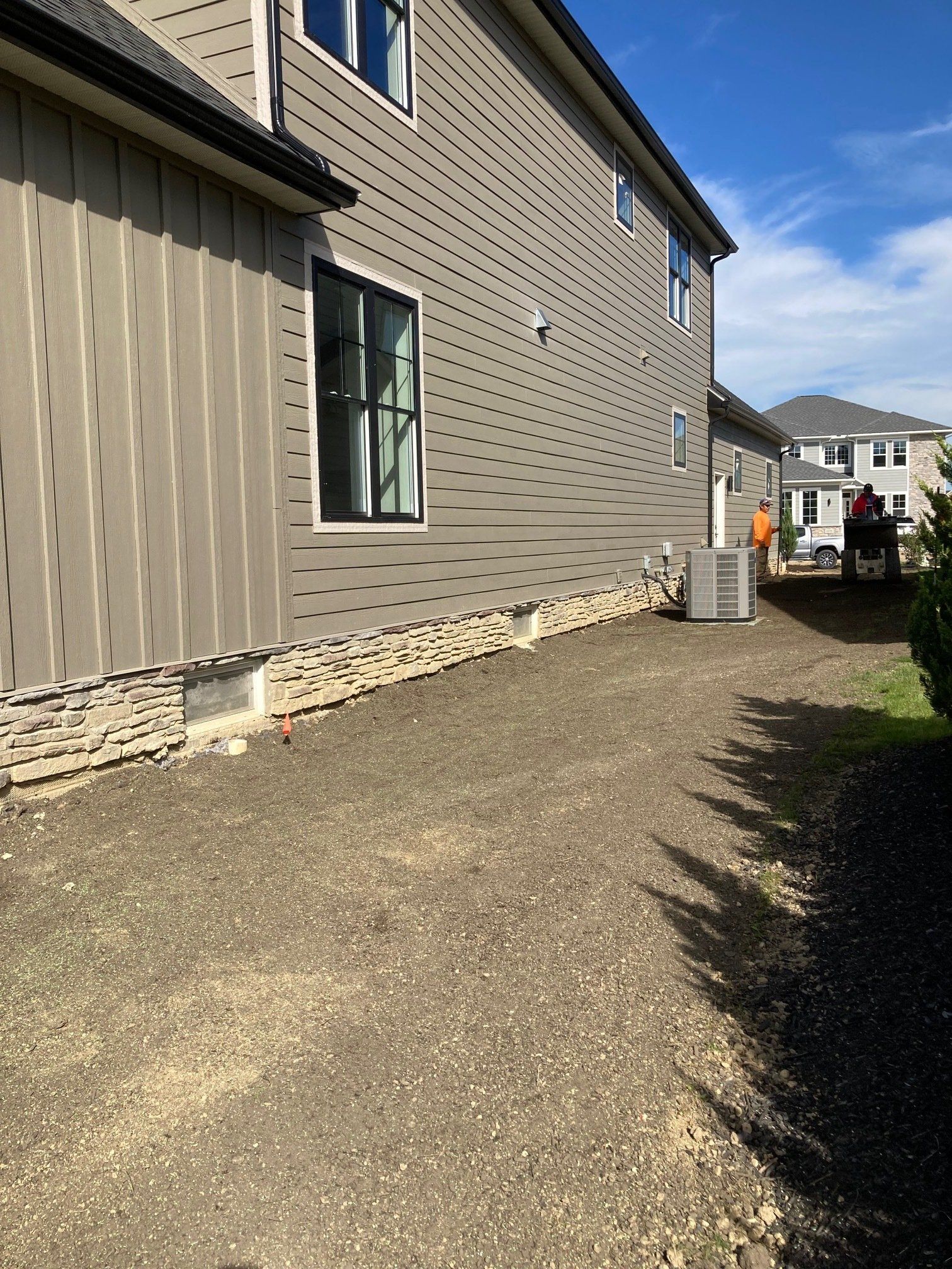 Side yard beside a tan house with gravel ground, a window, and a small patio area in sunlight