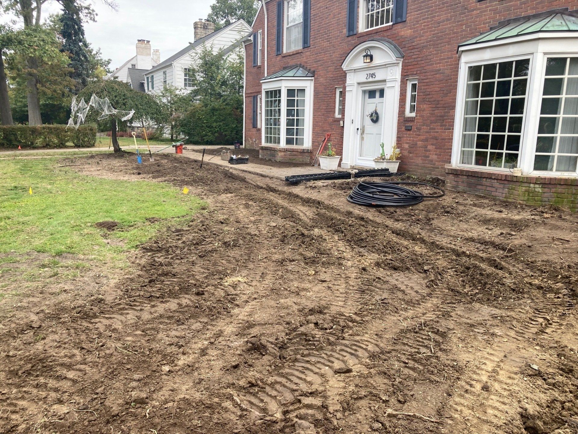 Front yard under renovation beside a brick house, with muddy ground and a curved dirt path.