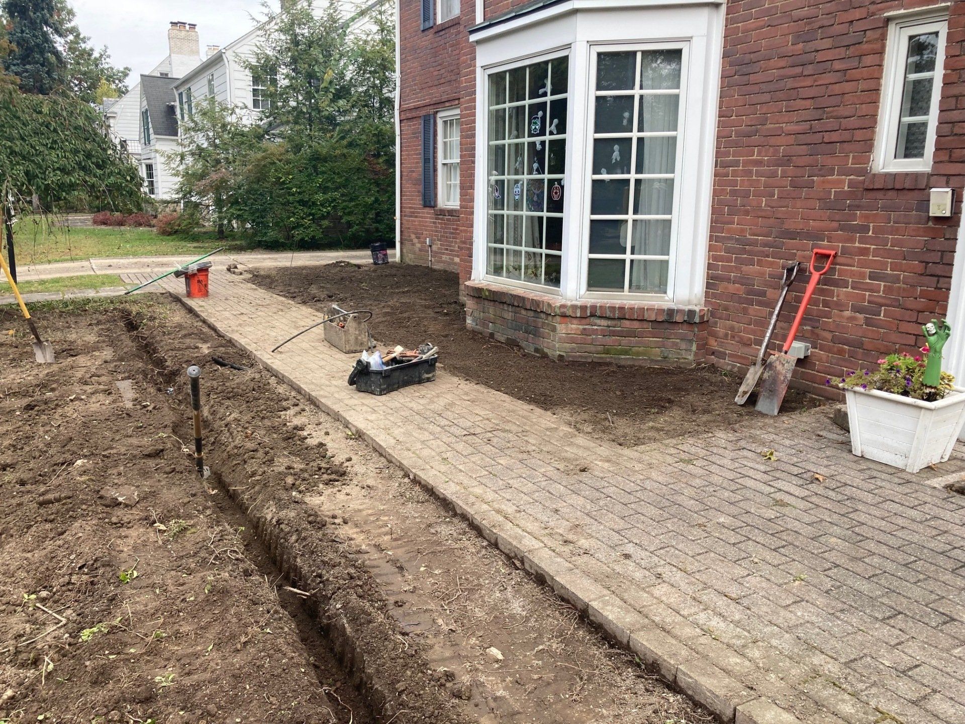 Backyard beside brick house with a new dug trench and paving stones, tools nearby