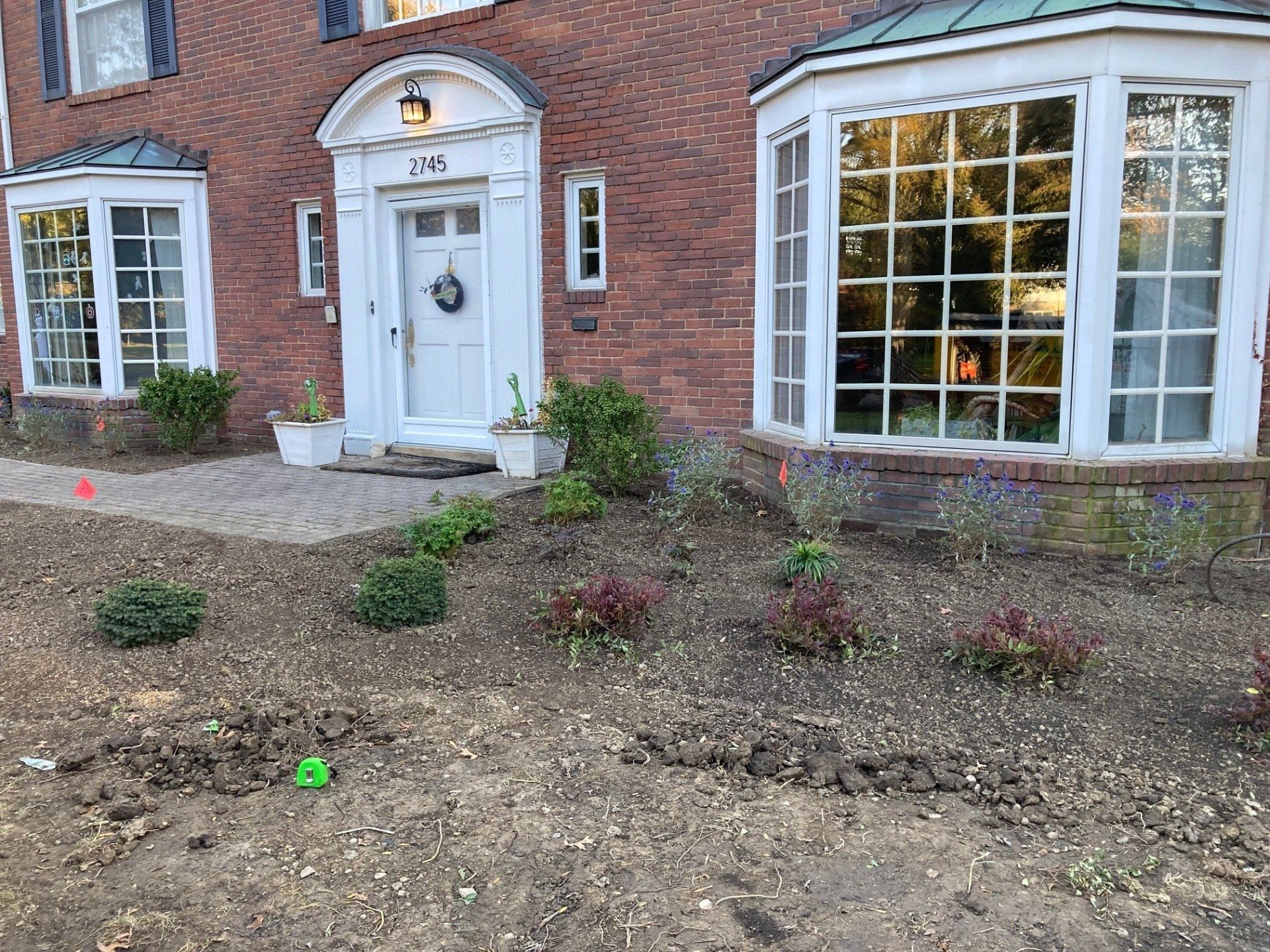 Brick house front entrance with white door, bay windows, and a bare front yard.