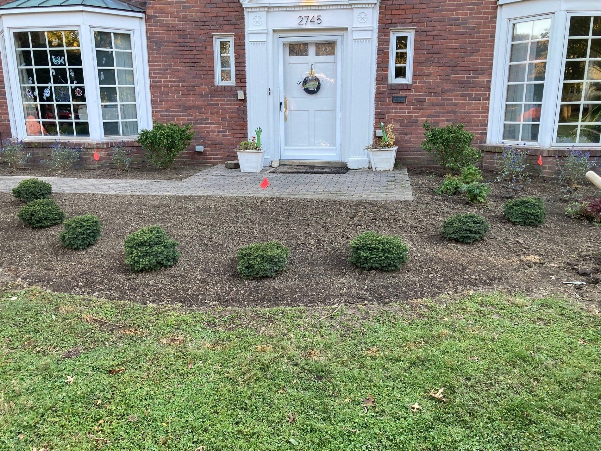 Brick house front entrance with white door, steps, and a newly landscaped front yard with shrubs.