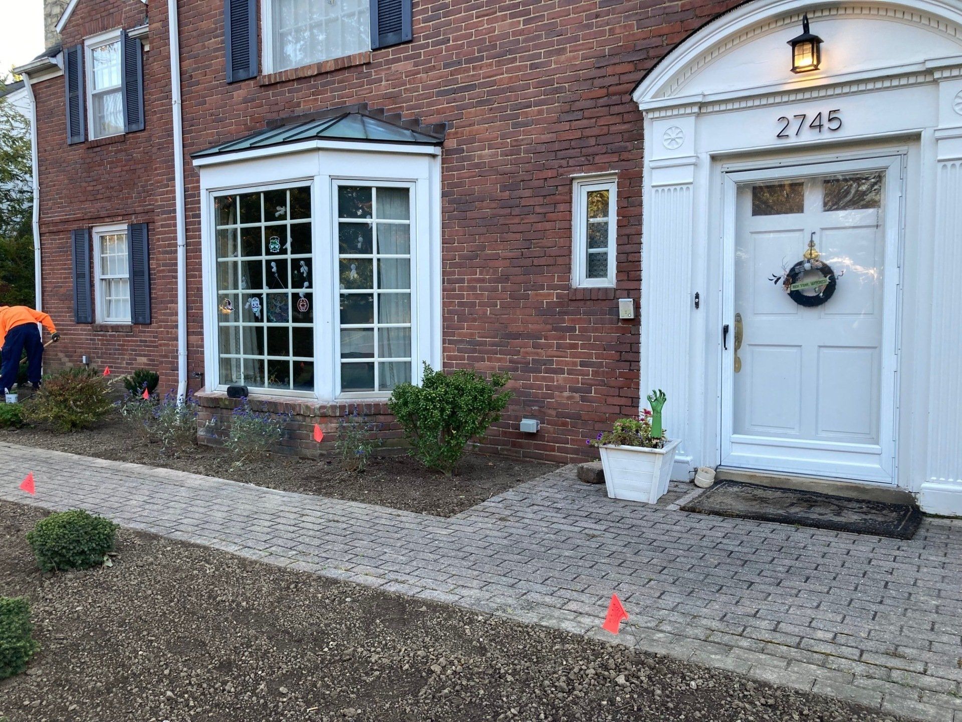 Brick townhouse entrance with white door, bay window, cobblestone path, and small potted plants