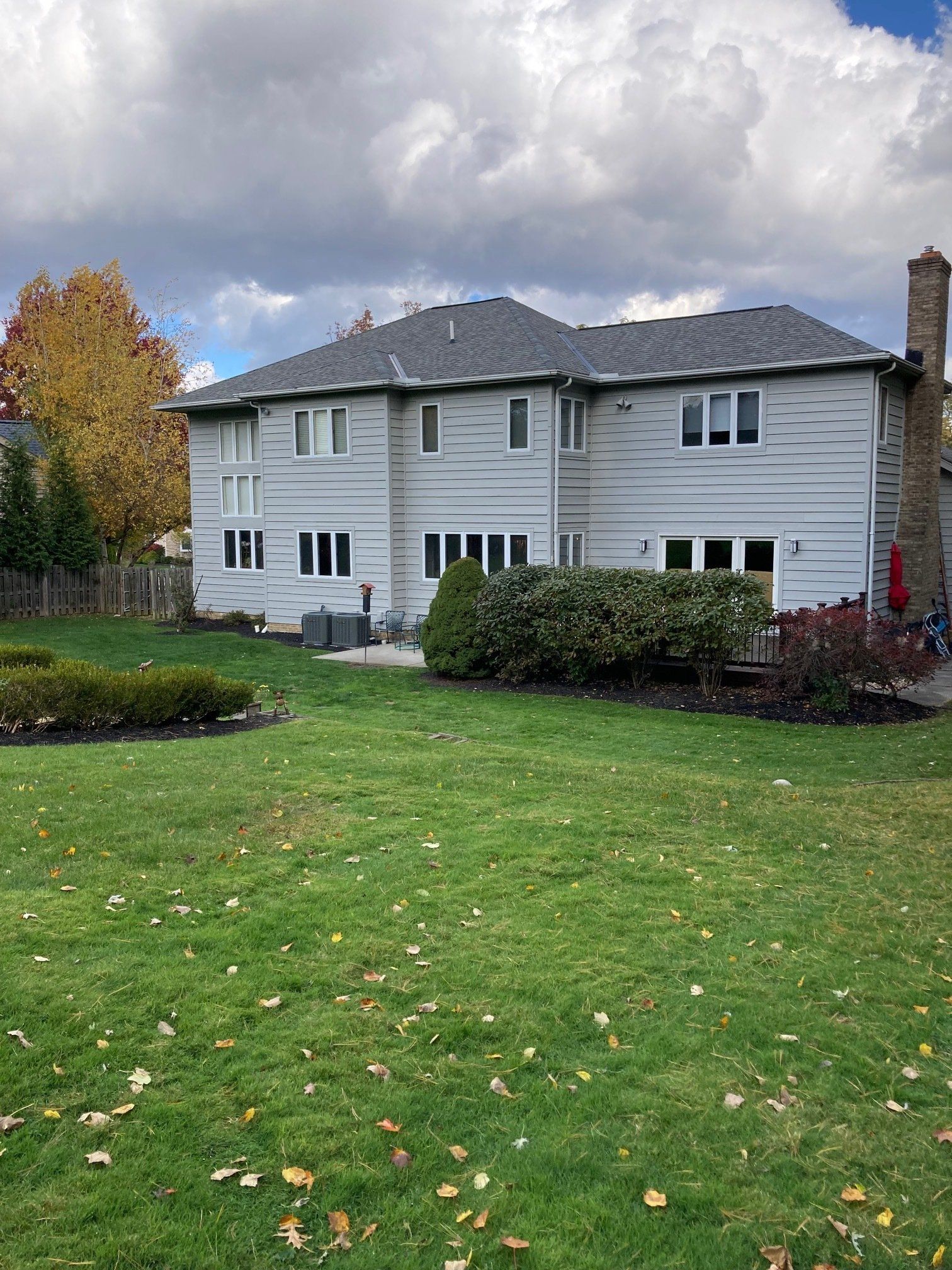 Two-story white house with black roof and green lawn under cloudy sky