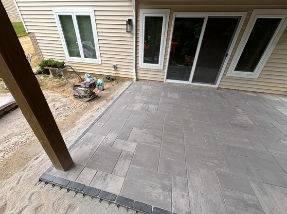Stone patio beside beige house with sliding glass doors and windows, under construction
