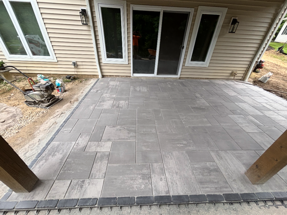 Gray paver patio beside a house, with sliding glass doors and steps in the foreground.