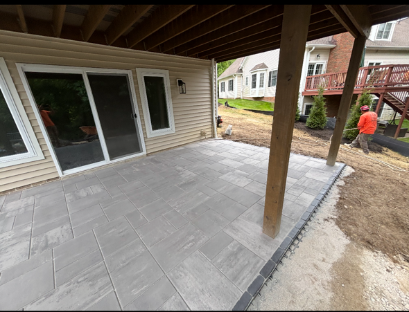 Covered patio with gray tile pavers and sliding glass doors beside a yard under construction