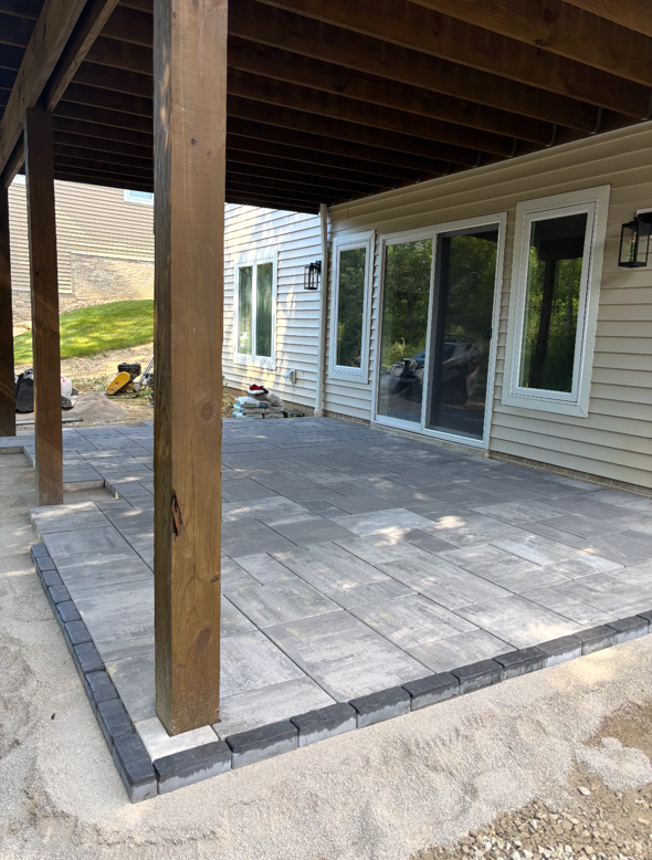 Covered patio with gray pavers, wooden post, and sliding glass doors on a house exterior