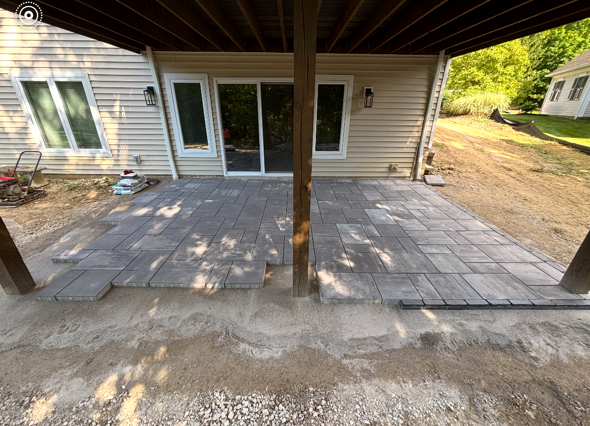 Covered patio with new gray pavers leading to sliding glass doors on a beige house