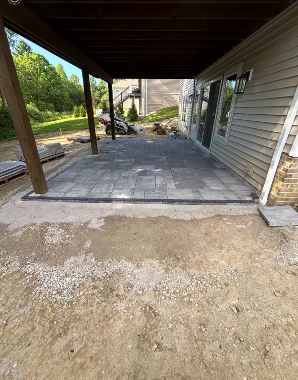 Covered patio with gray pavers beside a beige house and dirt yard under construction