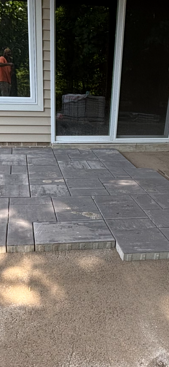 Stone patio with large gray pavers leading to glass sliding doors beside a house siding wall