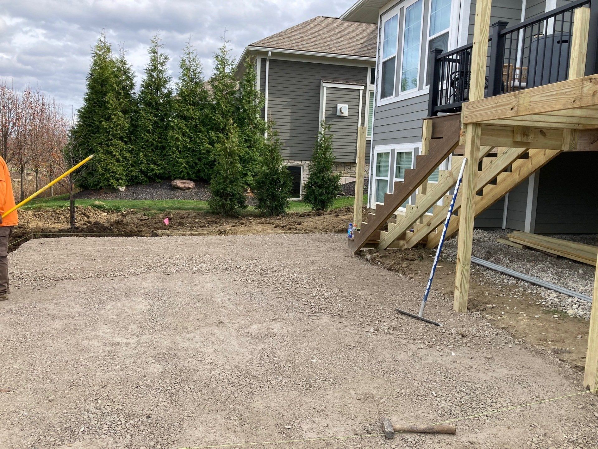 Gravel backyard beside a house with stairs, trees, and two tools on the ground
