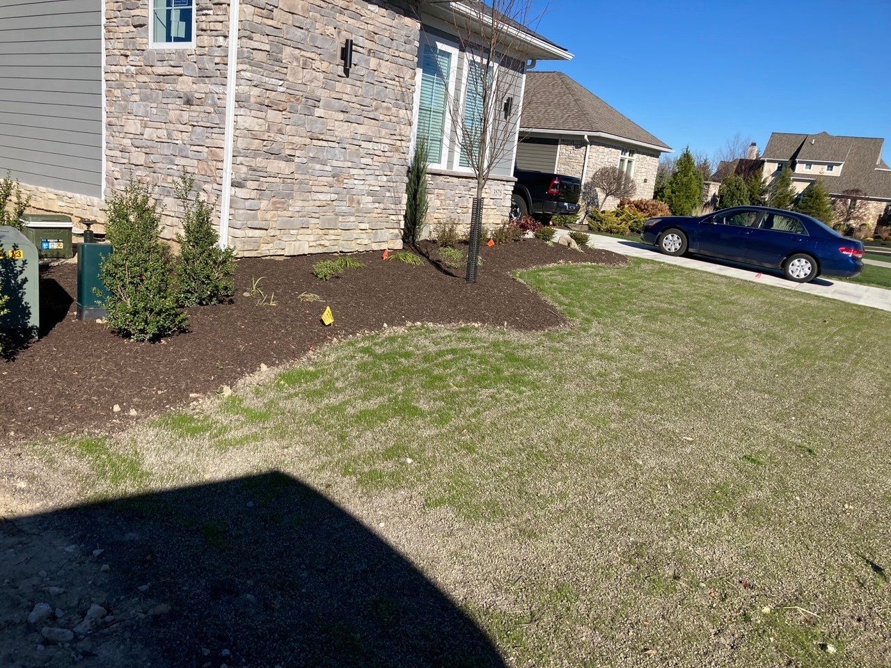Suburban house with stone exterior, front lawn, shrubs, and a blue car parked in the driveway.