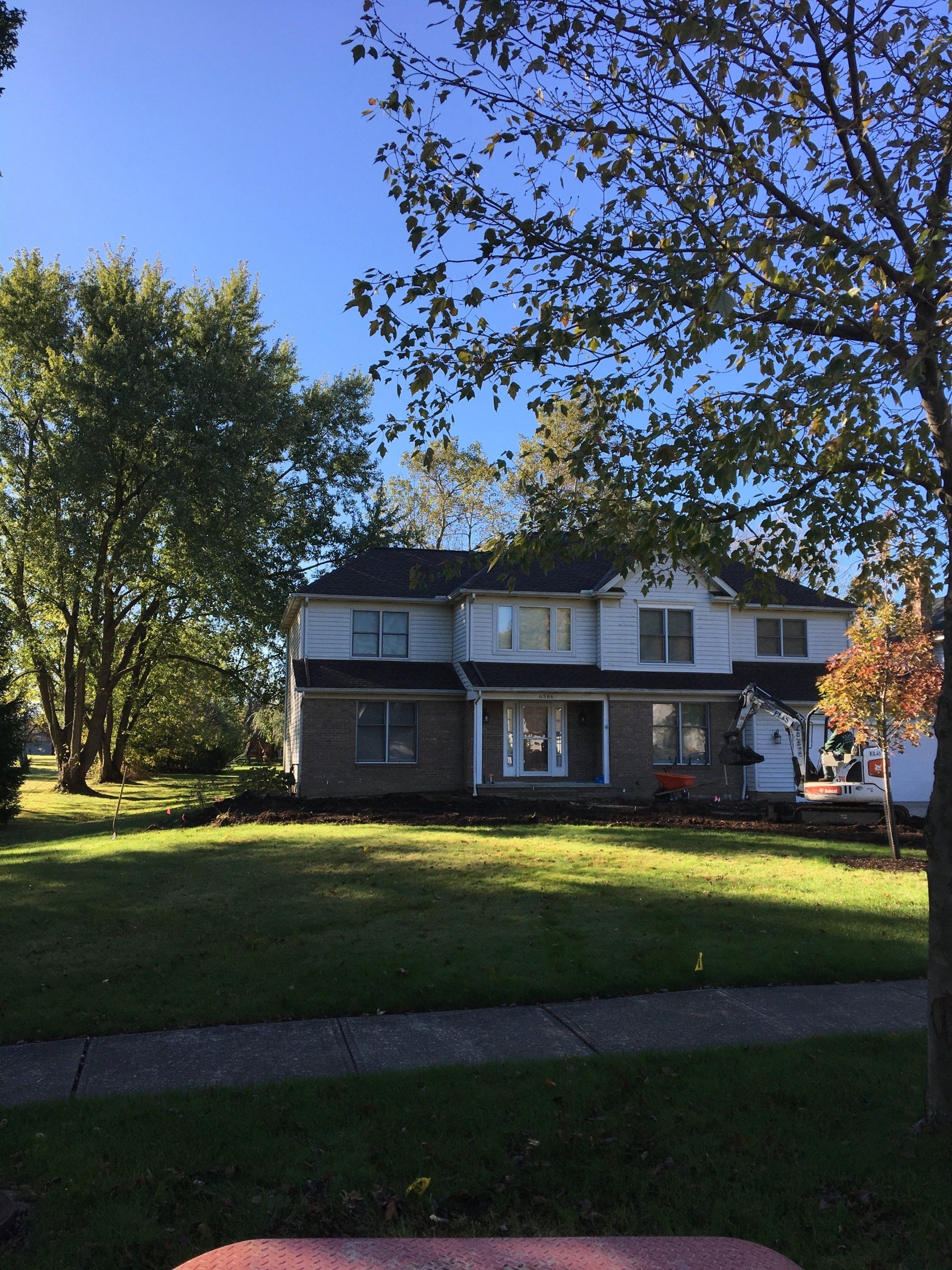 Two-story house with a front lawn and large trees in bright sunlight