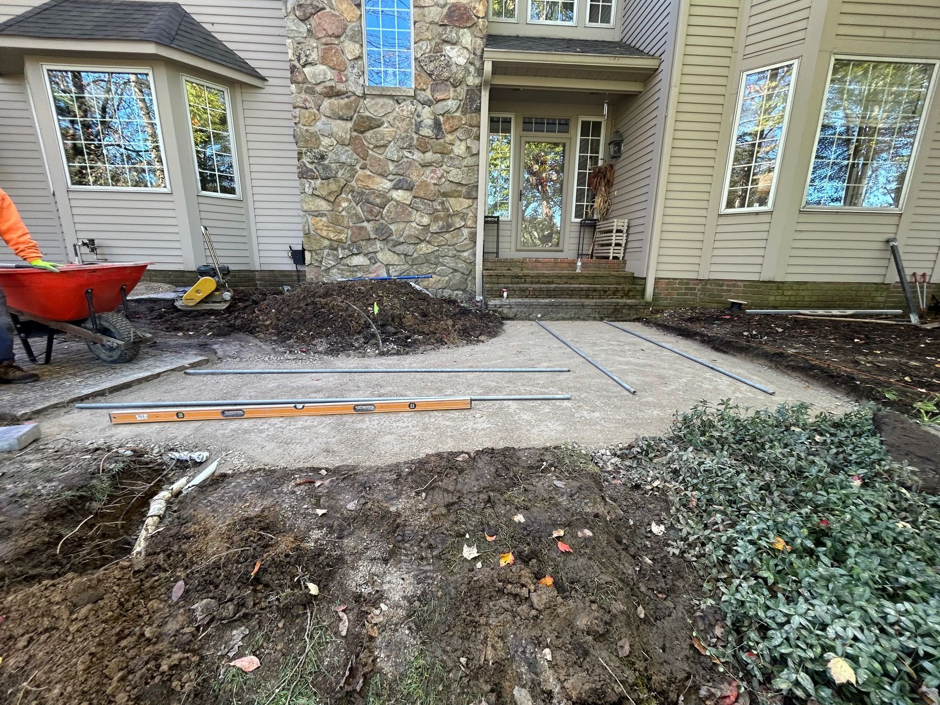 Front yard walkway under construction with dirt piles, a wheelbarrow, and stone house entrance