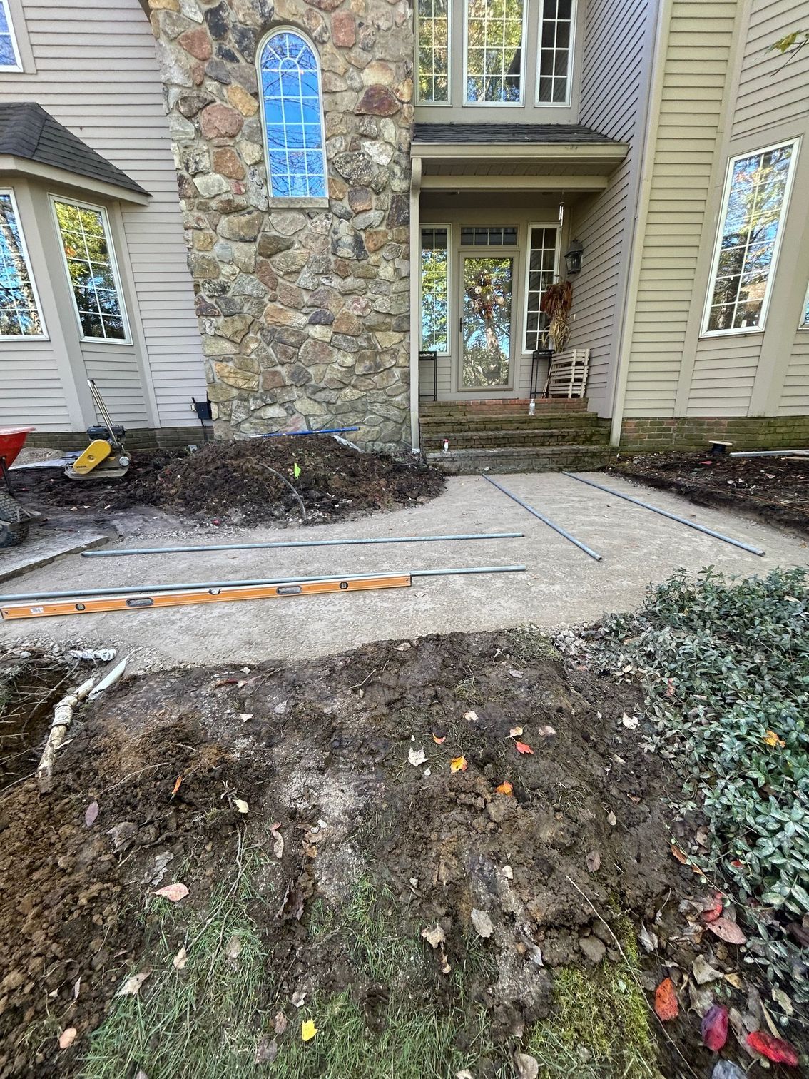 Front entrance walkway to a stone-and-siding house with muddy, damaged landscaping and steps.