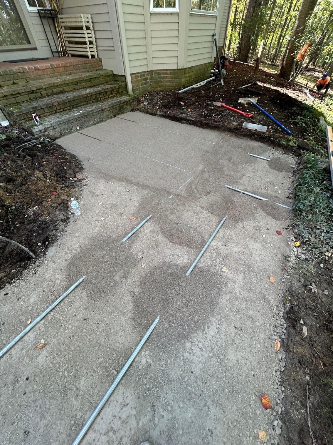 Concrete walkway beside a house, with blue tape/strips marking cracks and uneven patches.
