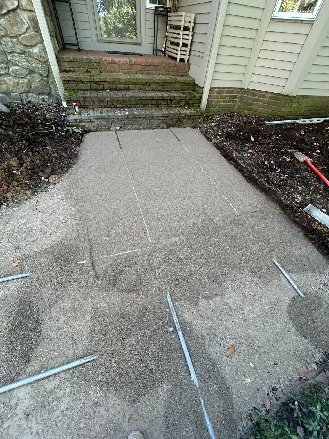 Uneven concrete walkway leading to front steps, with visible seams and garden edging on both sides.