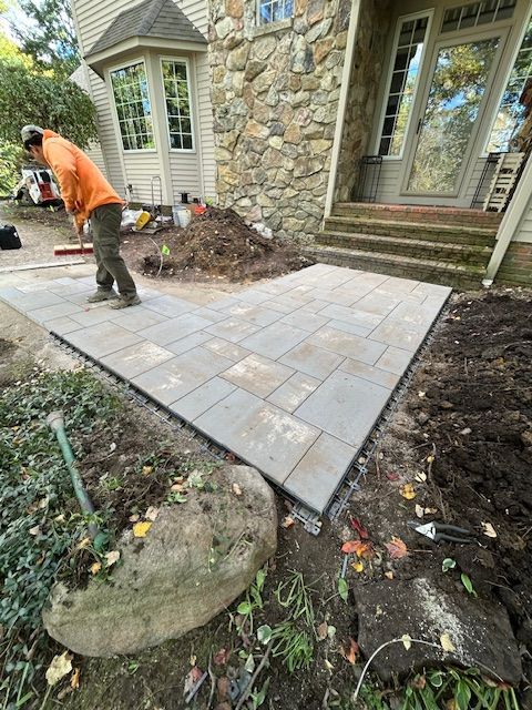 Worker laying paver patio beside stone house and garden bed