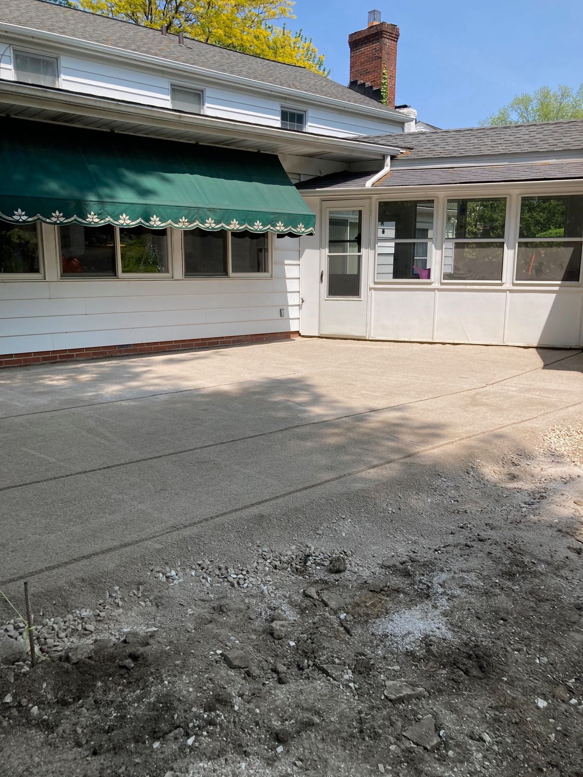 House exterior with awnings and a paved courtyard, showing a cracked patch in the foreground.