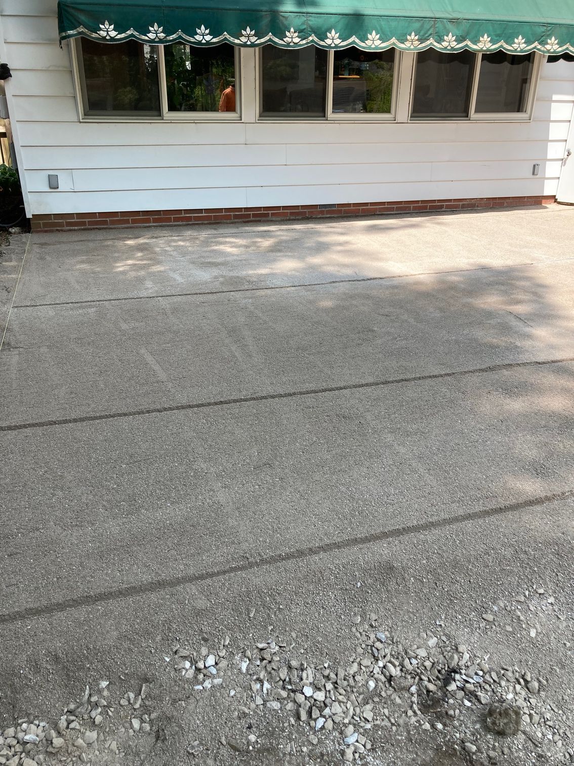 Cracked asphalt driveway with potholes in front of a white house with windows and a scalloped awning