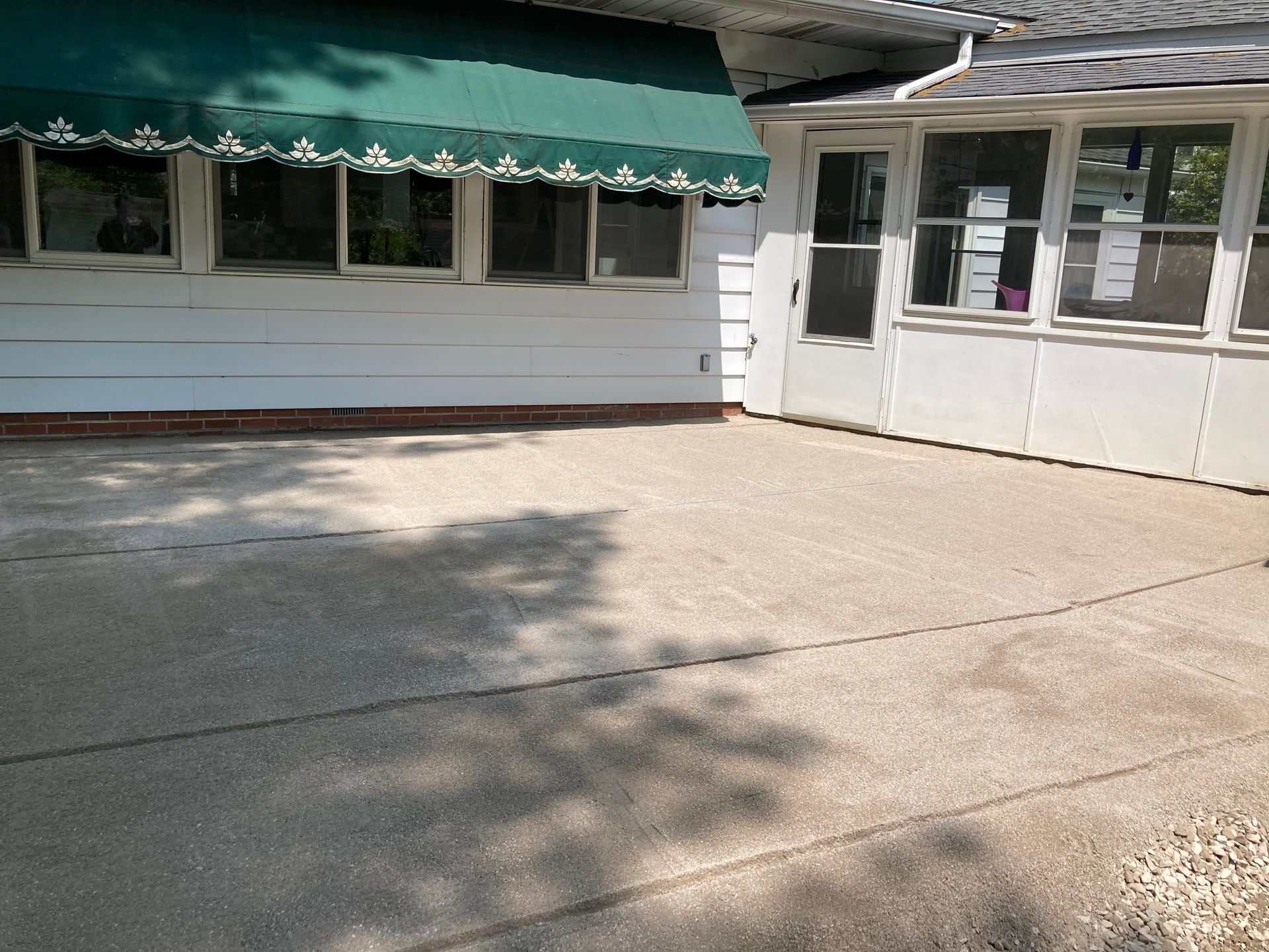 White building with green awning and windows beside a sunlit concrete courtyard